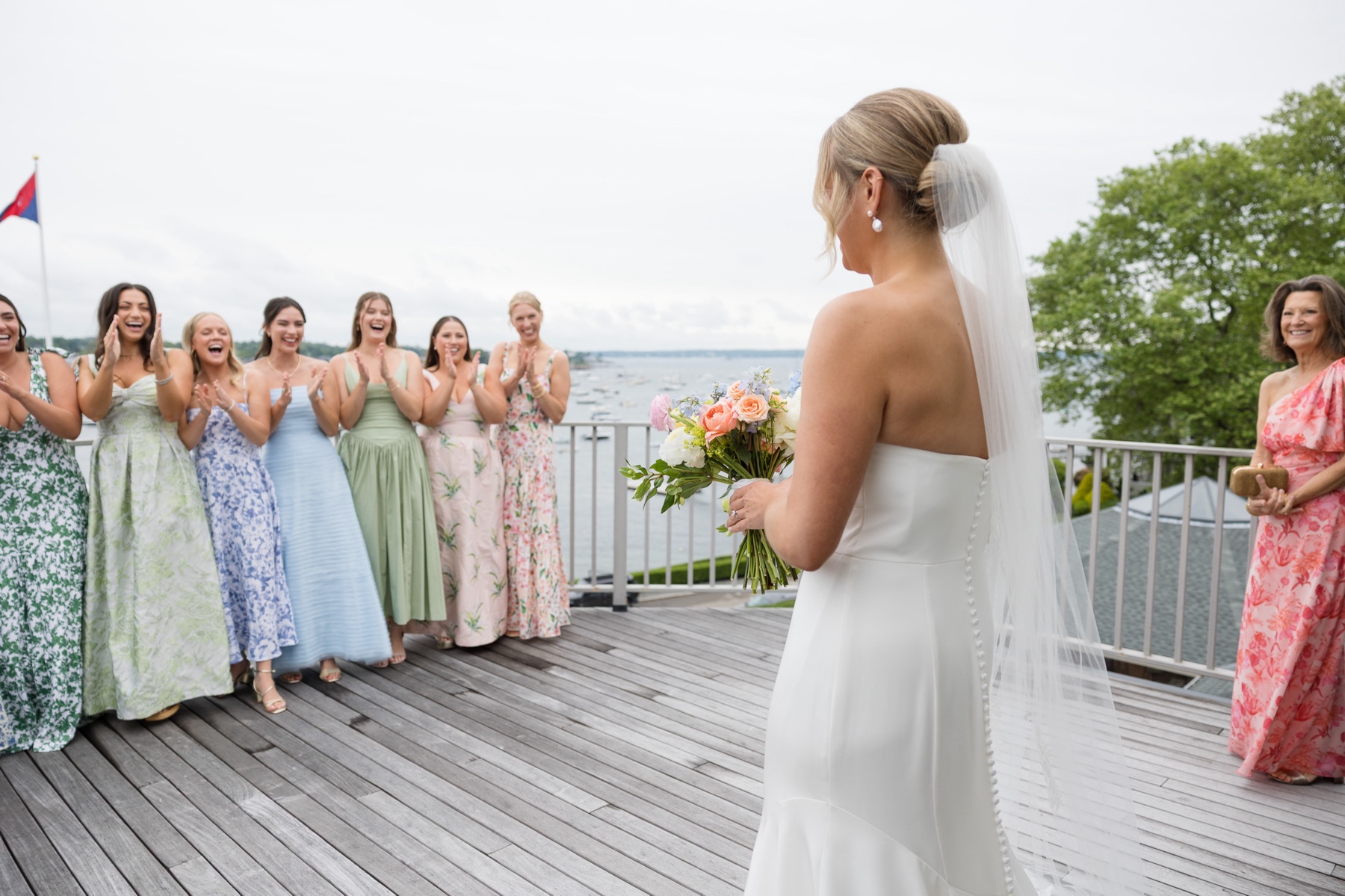 bride standing on deck for first look with bridesmaids wearing floral dreses
