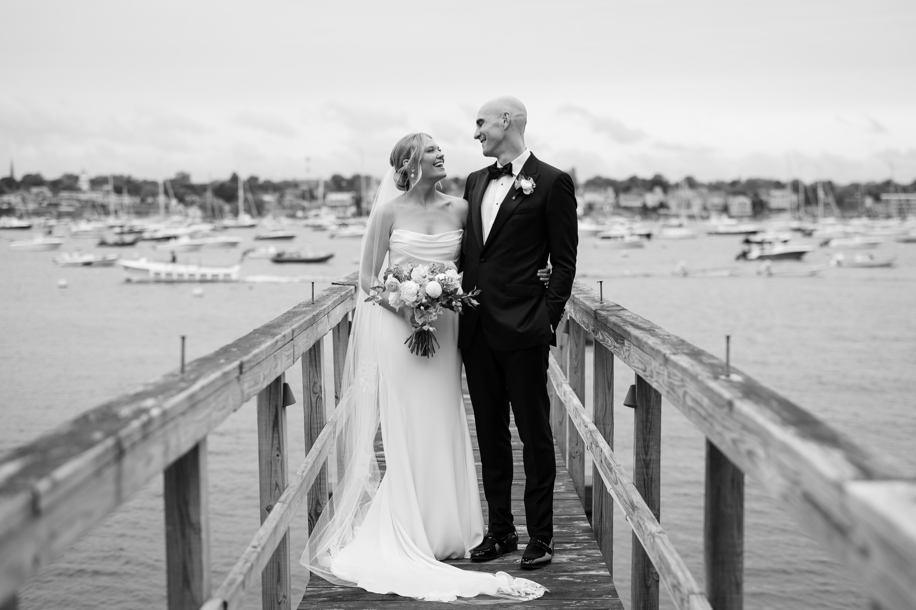 bride and groom standing on the eastern yacht club dock smiling at each other